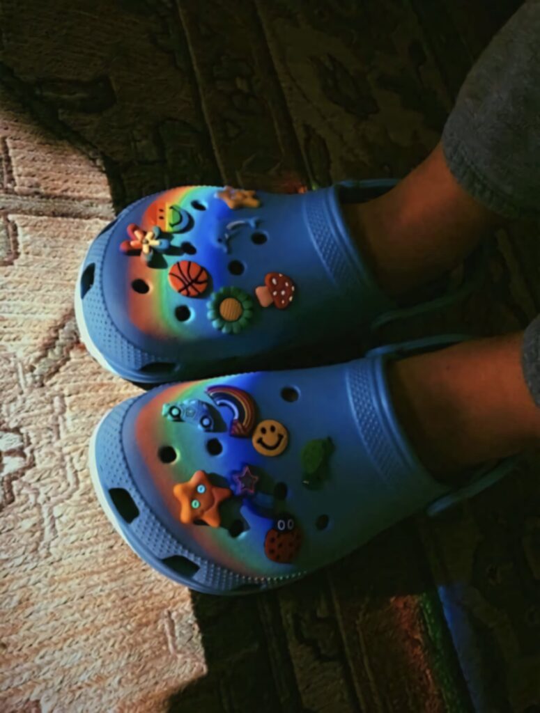 Cozy blue Crocs with colorful rainbows stars and smiley charms on patterned rug background Wallpaper