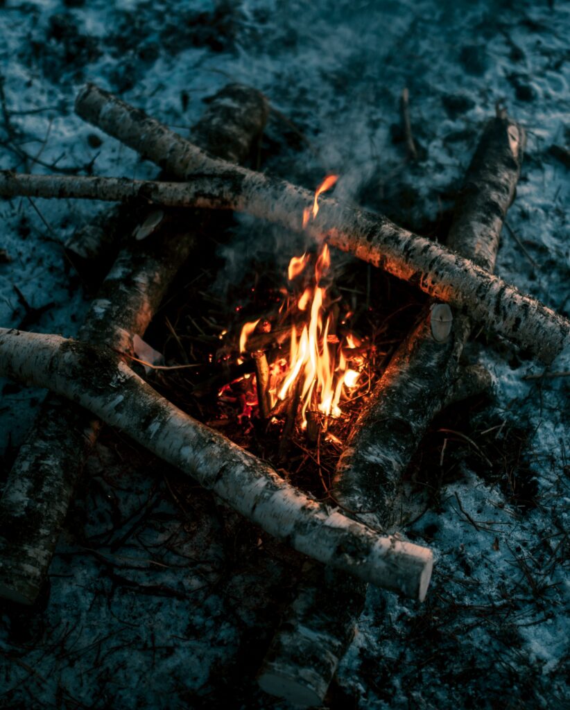 Cozy bonfire with orange flames on snowy ground surrounded by wooden logs in rustic outdoors Wallpaper
