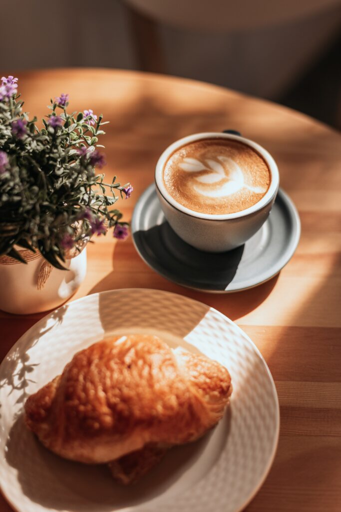 Cozy Breakfast Scene: Cappuccino & Croissant on Wooden Table Wallpaper