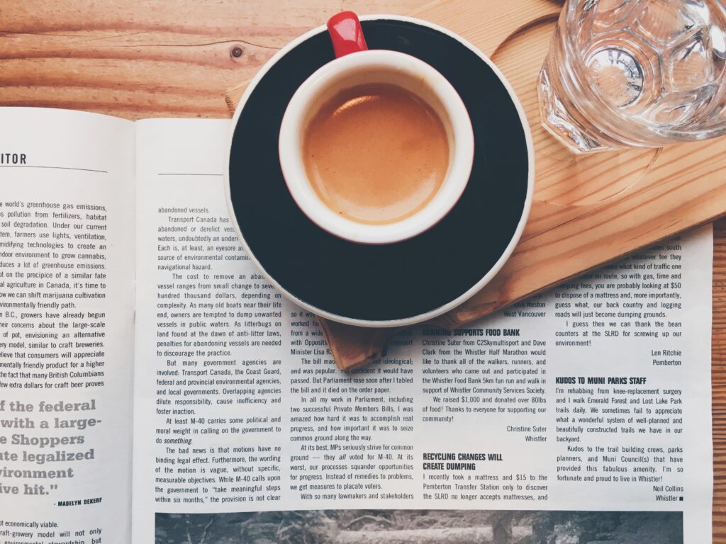 Cozy Breakfast Scene: Coffee, Newspaper & Water on a Wooden Table Wallpaper