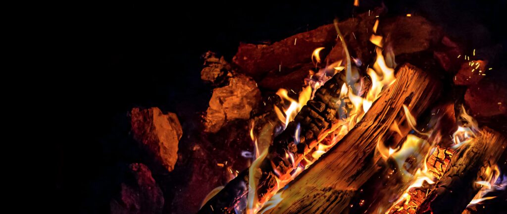 Campfire flames glow on rugged rocks and logs under a starry night sky outdoor wallpaper