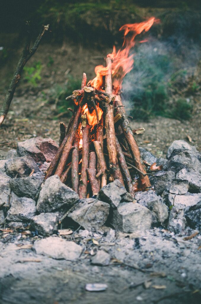 Cozy camping bonfire with bright flames on stacked logs and rustic stone ring outdoor wallpaper