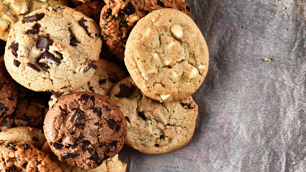 Close-up of golden brown chocolate chip and nut cookies on rustic parchment paper background Wallpaper