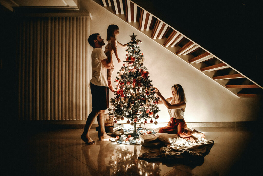 Cozy Family Christmas: Decorating a Tree Amidst Festive Glow Wallpaper