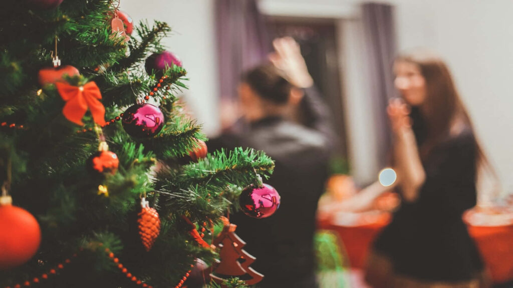 Cozy Holiday Gathering with Brightly Decorated Christmas Tree Wallpaper
