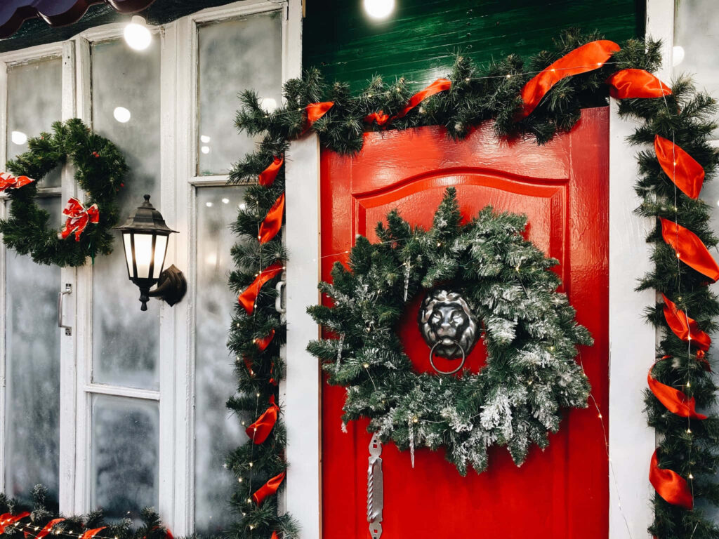 Cozy Christmas Scene: Red Door with Wreath & Warm Lantern Glow Wallpaper