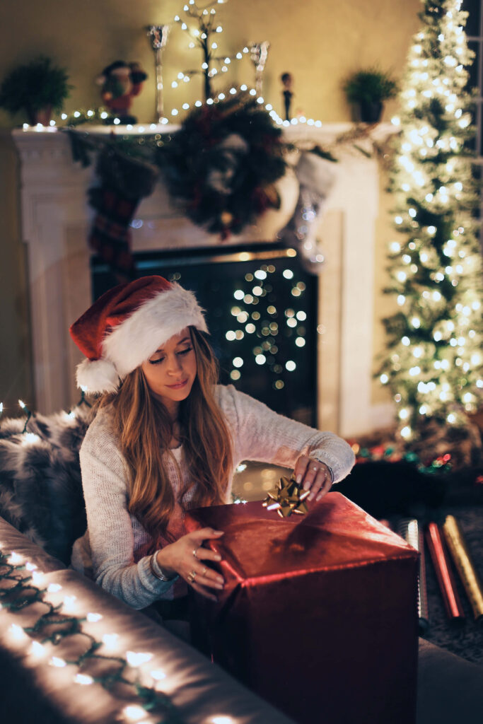 Cozy Christmas Scene: Woman in Santa Hat Unwrapping Gifts Wallpaper