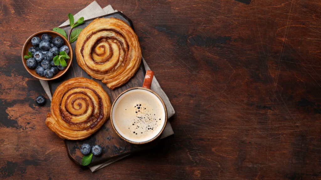 Cozy breakfast wallpaper with golden cinnamon rolls coffee and fresh blueberries on wood