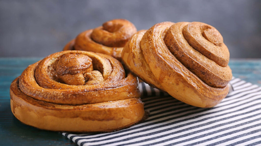 Fresh baked cinnamon rolls with golden swirls on rustic wood and striped cloth background Wallpaper