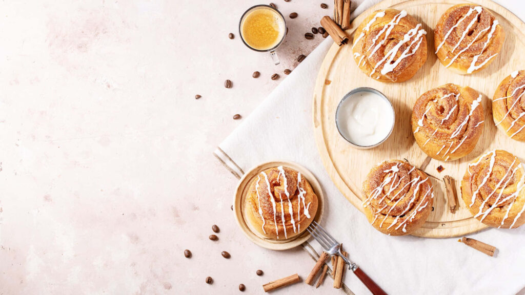 Freshly baked cinnamon rolls with icing and coffee beans on wooden board cozy breakfast Wallpaper