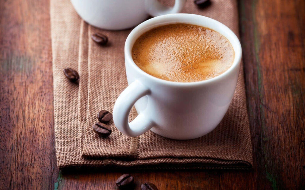 Close-up of white ceramic cup with frothy coffee on rustic table with coffee beans and cloth Wallpaper