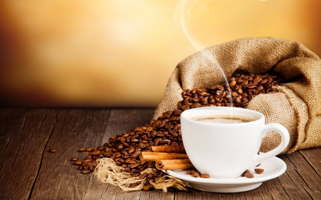 Steaming white coffee cup with cinnamon sticks and roasted beans on rustic wooden table wallpaper