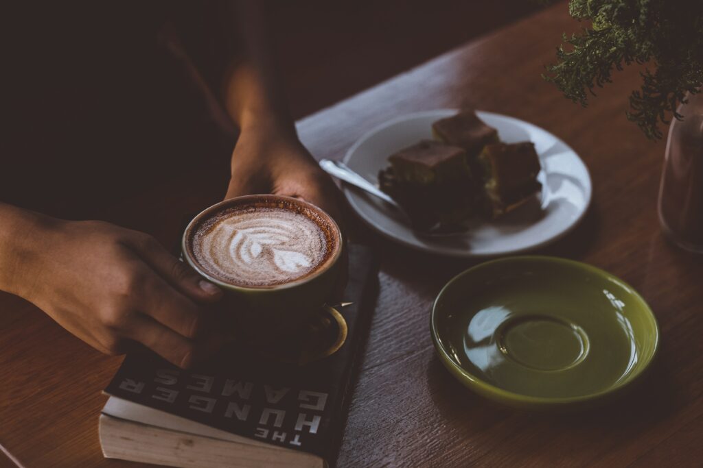 Cozy Coffee Scene: Hands, Latte Art, and Snacks on Wooden Table Wallpaper