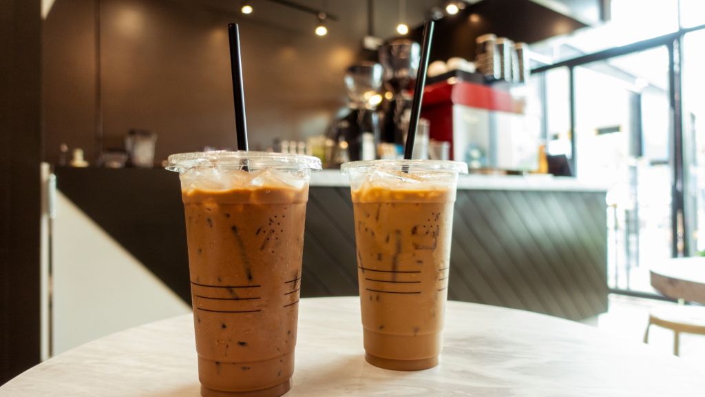 Cozy coffee shop wallpaper with two iced lattes on white marble table and warm blurred cafe background