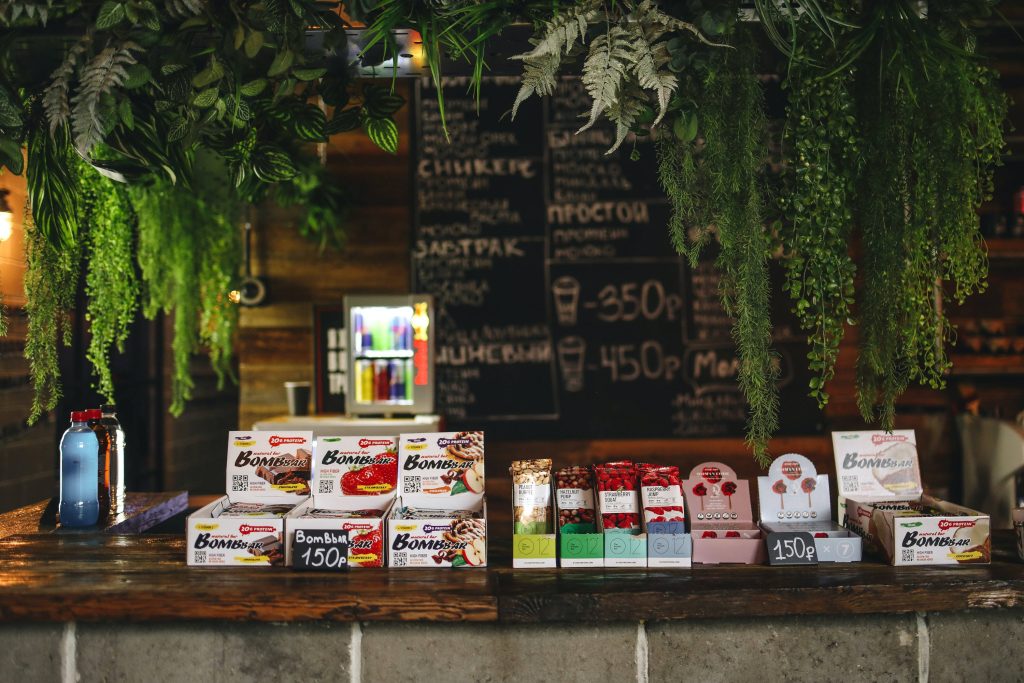 Cozy coffee shop wallpaper with rustic wooden counter Bombbar protein bars lush plants warm lighting