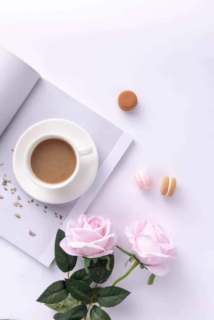 Elegant coffee cup on open book with pink roses and macarons pastel serene wallpaper background