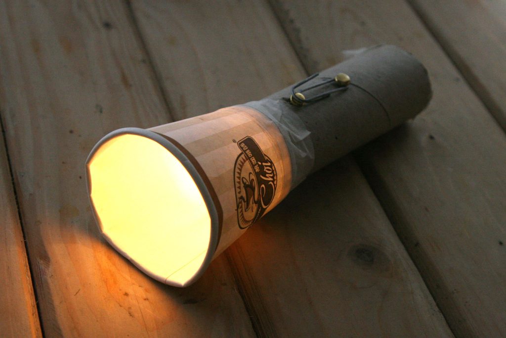 DIY flashlight made from paper cup and cardboard glowing warmly on rustic wooden planks background Wallpaper
