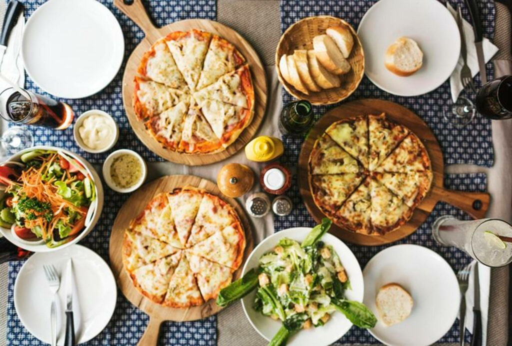 Cozy Dinner Scene Wallpaper: Pizzas, Salads, and Beverages