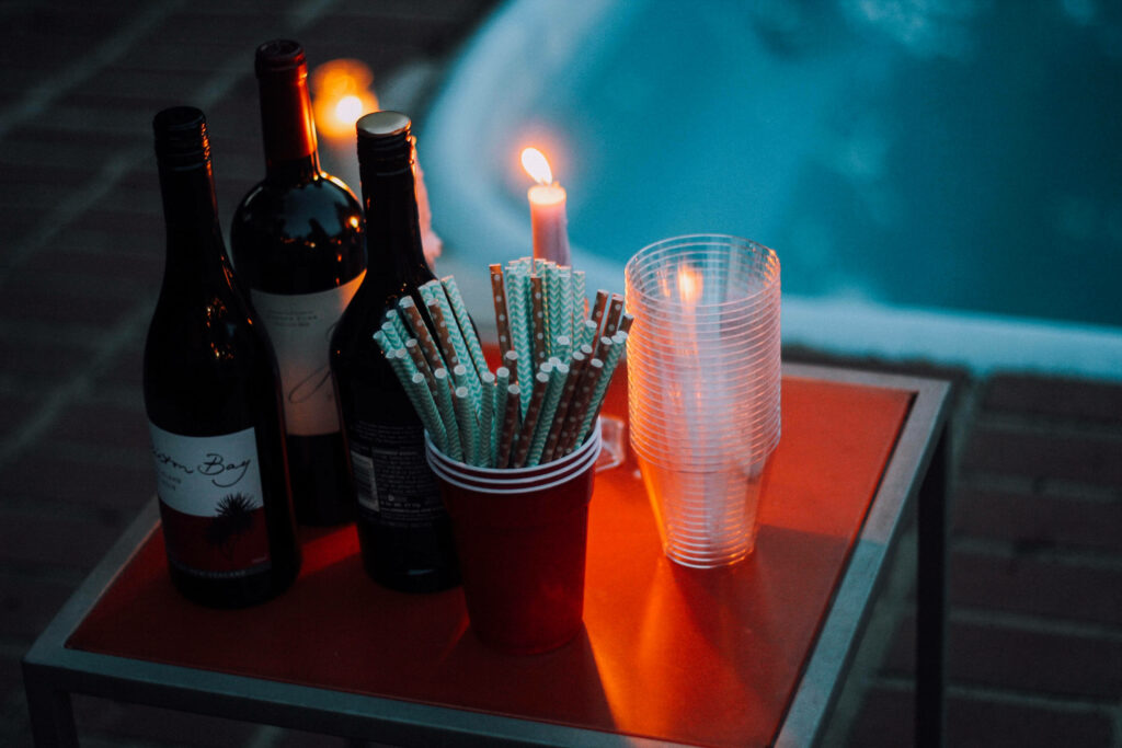 Orange table with wine bottles candles and cups beside pool at dusk warm cozy evening scene Wallpaper