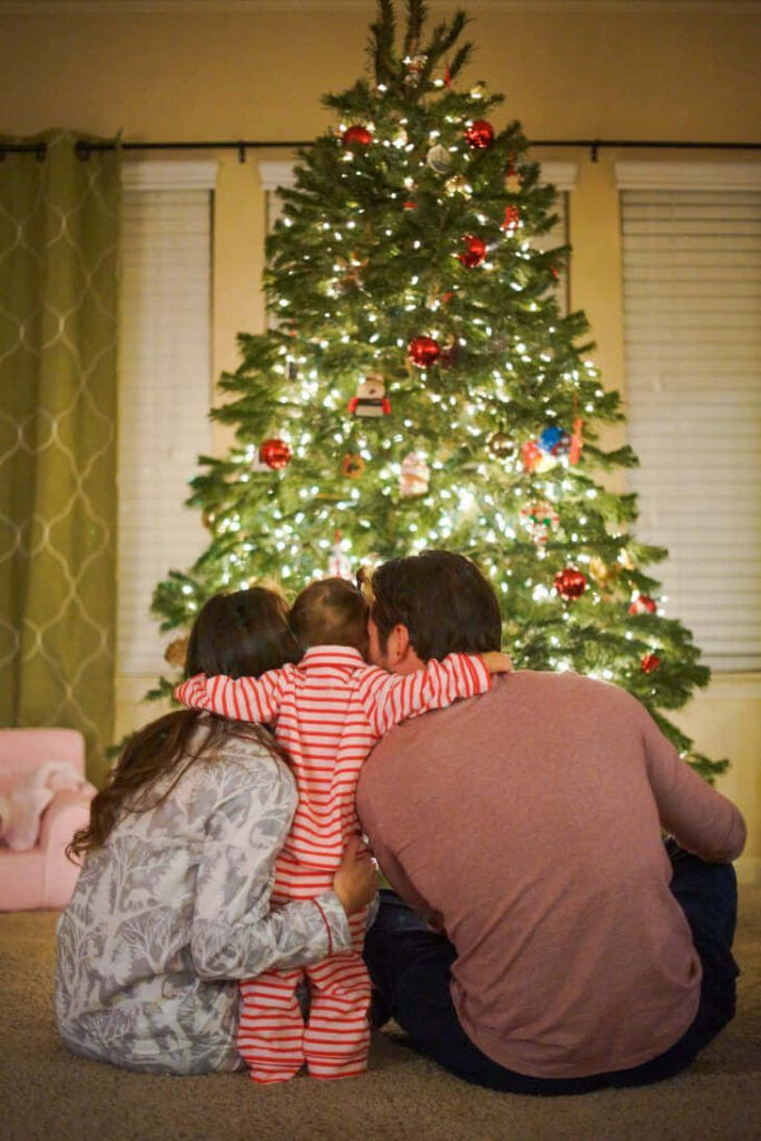 Cozy Family Embrace by a Festive Christmas Tree Wallpaper