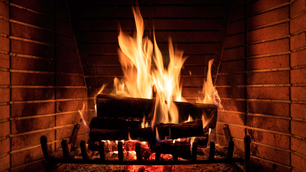 Cozy glowing fireplace with burning logs behind steel bars warm inviting Zoom background wallpaper