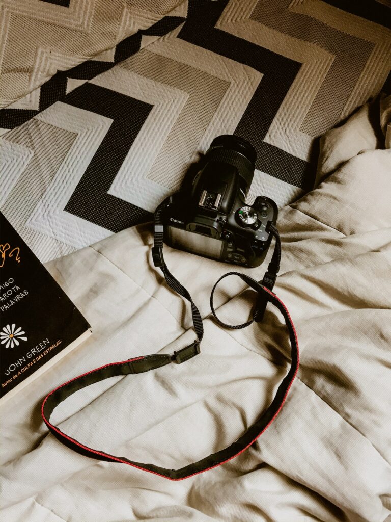 Cozy Flat-Lay: Black DSLR Camera, Book & Soft Bedding Ambiance Wallpaper