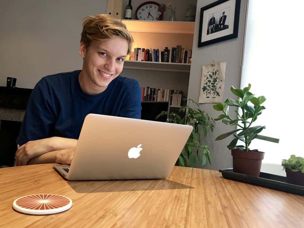 George Ezra smiling working on laptop cozy plant-filled home office natural light wallpaper