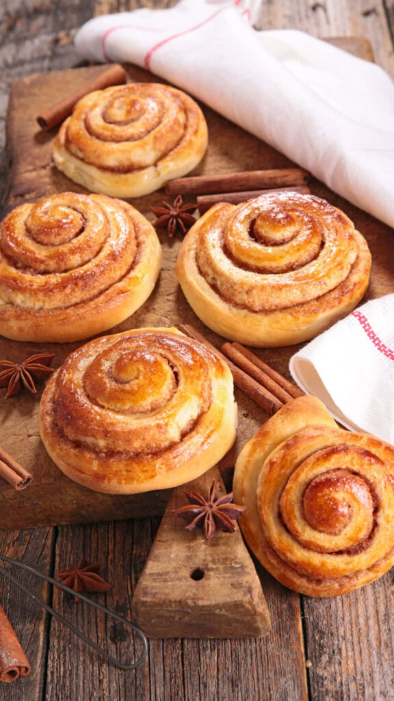 Warm golden cinnamon rolls with glossy glaze on rustic wood with cinnamon sticks and star anise Wallpaper