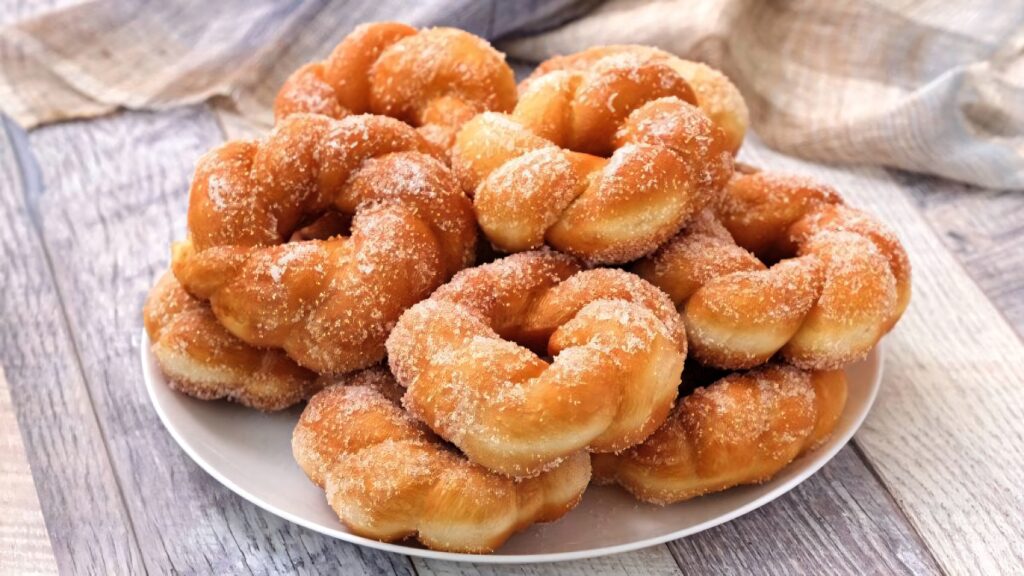 Golden sugar-coated twisted donuts stacked on plate cozy rustic wooden table wallpaper background