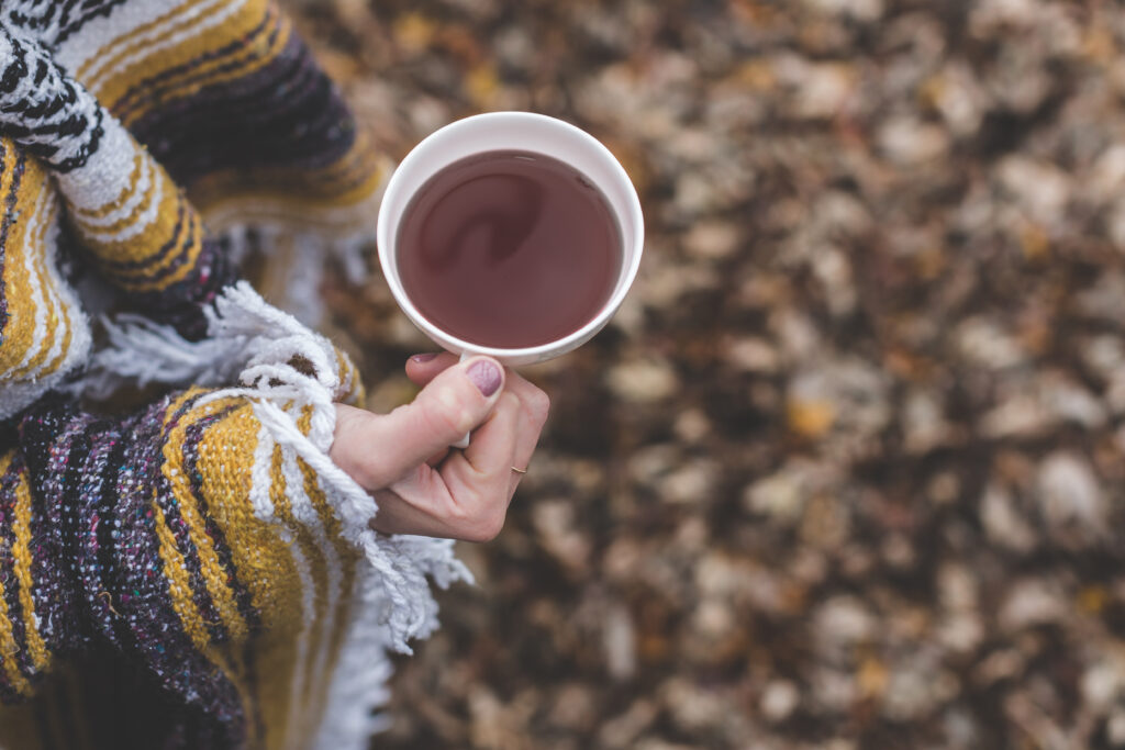 Cozy Hand in Striped Jacket with Tea Amidst Autumn Leaves Wallpaper