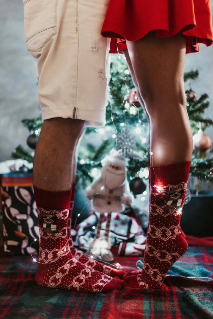 Cozy Holiday Scene: Couple by Christmas Tree in Cheerful Socks Wallpaper