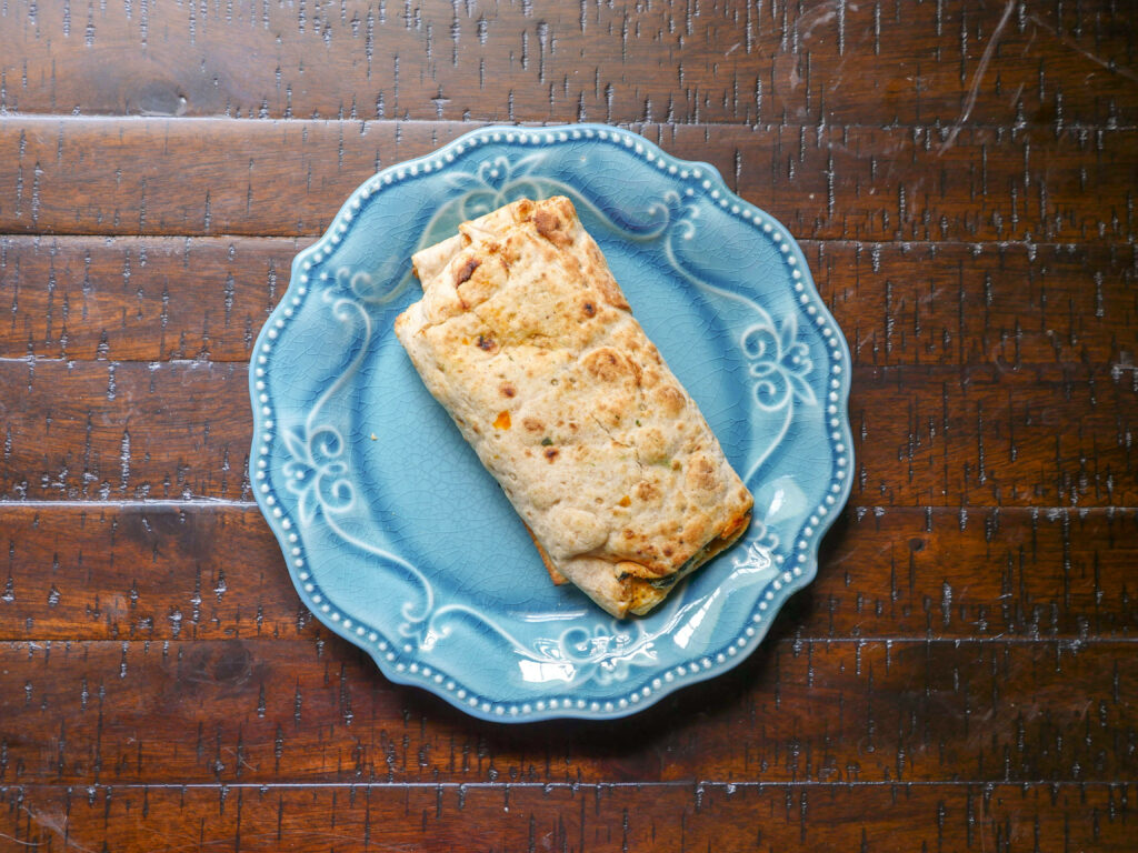 Golden brown burrito on blue plate rustic wooden table cozy kitchen natural warm light Wallpaper