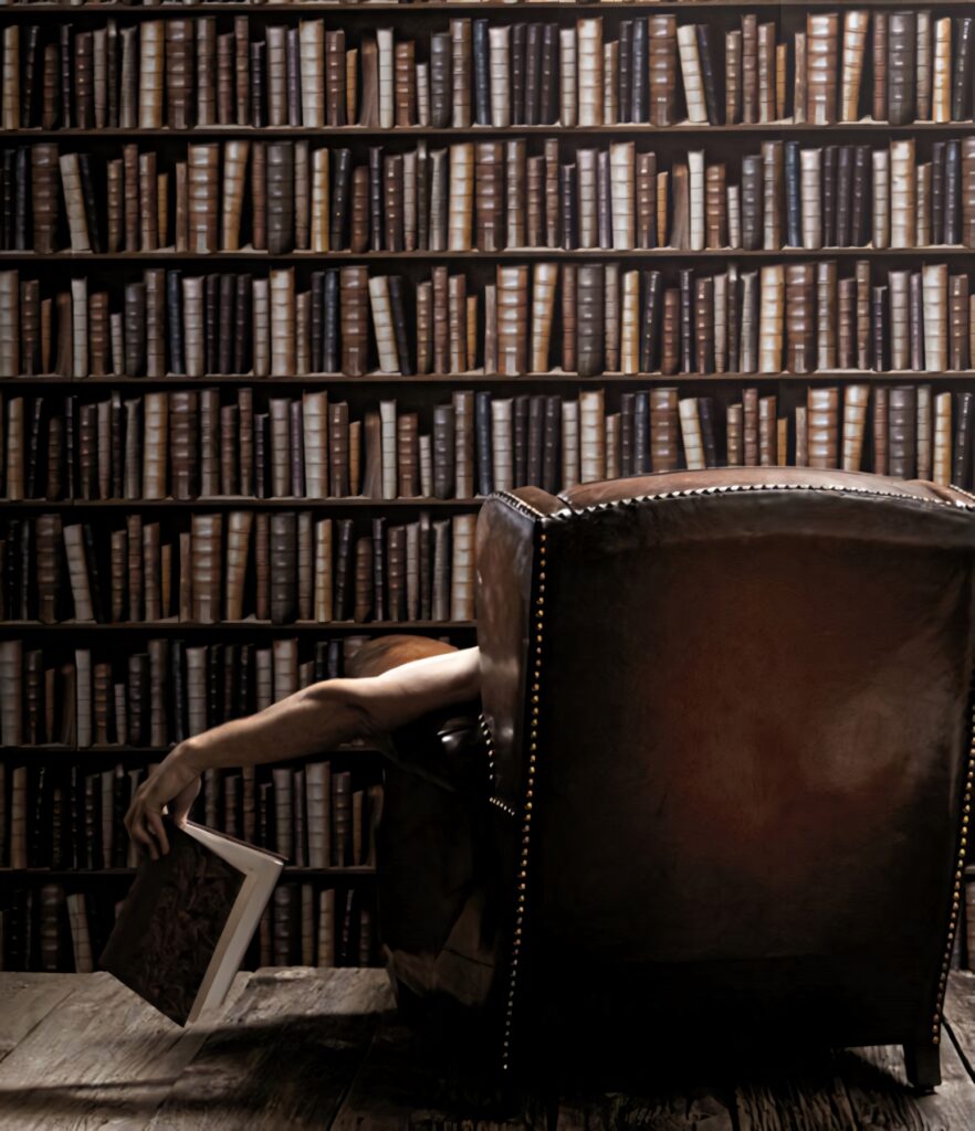 Man in leather chair reaching for book on large bookshelf wall cozy intellectual study room Wallpaper