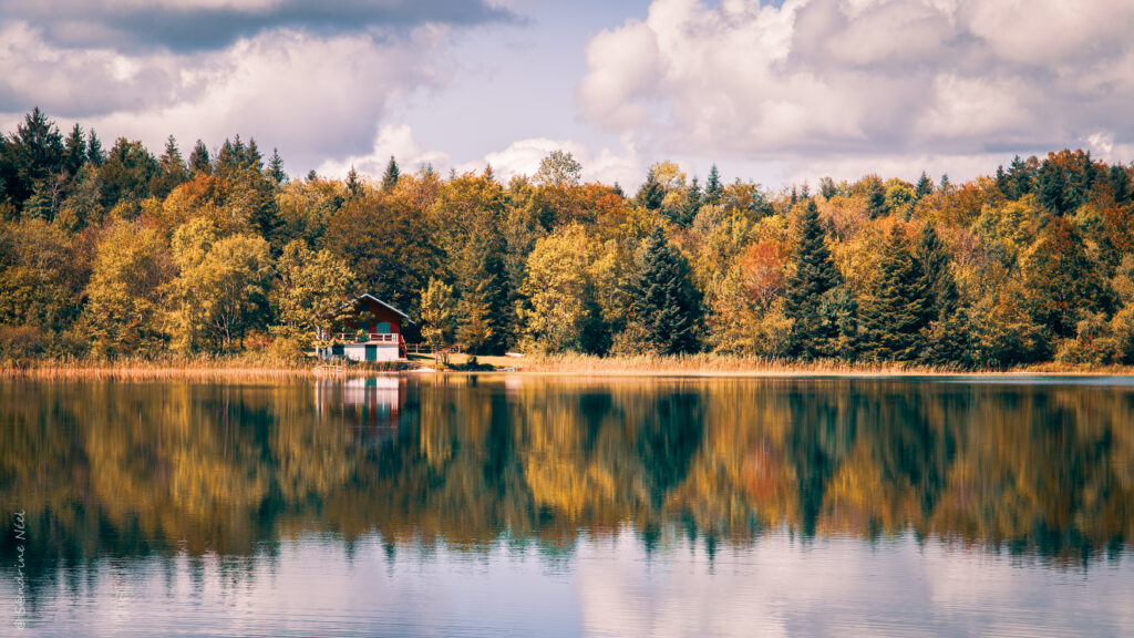 Cozy house by tranquil lake with autumn trees and clear reflections serene nature wallpaper