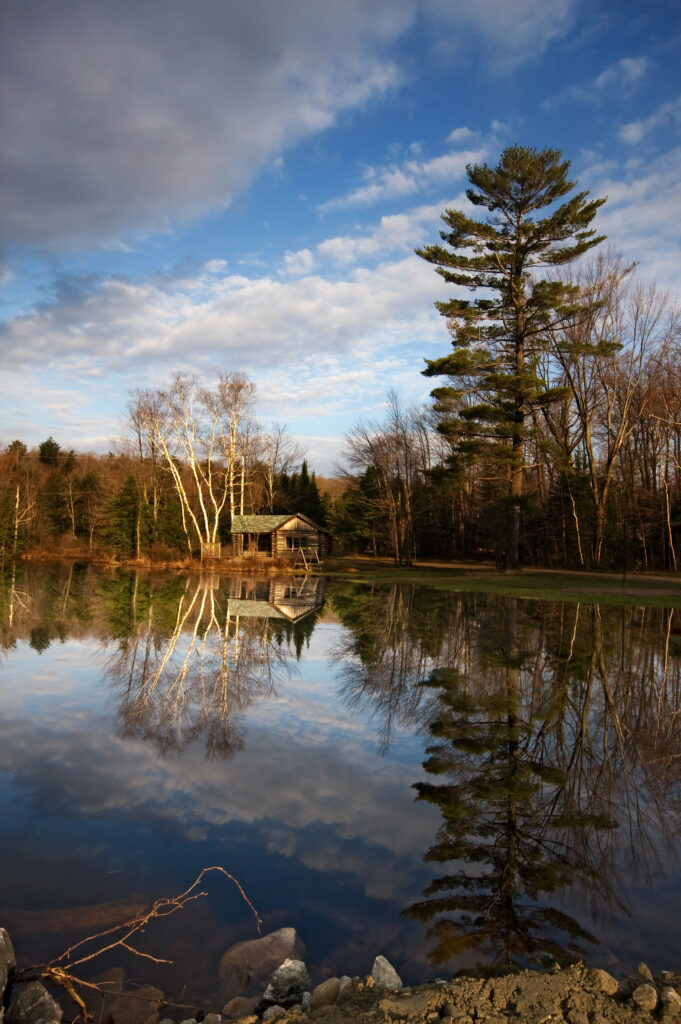 Cozy house by peaceful lakeside reflecting forest trees sky and warm sunlight nature wallpaper