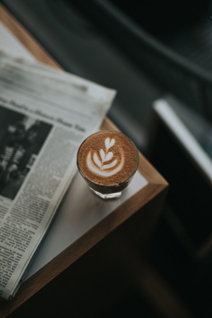 Cozy Latte Scene: Close-Up of Craftsmanship with Newspaper Background Wallpaper