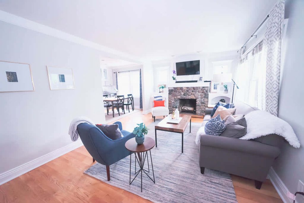 Cozy living room virtual Zoom wallpaper with rustic fireplace grey couch blue armchair hardwood floors