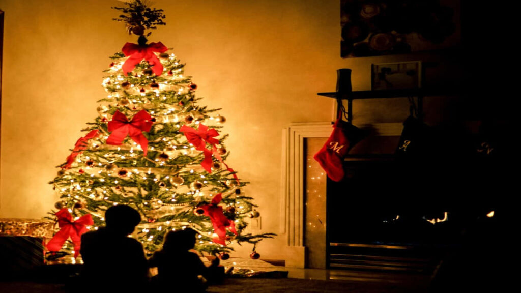 Festive Christmas Tree Shines in Cozy Living Room with Silhouetted Figures Wallpaper