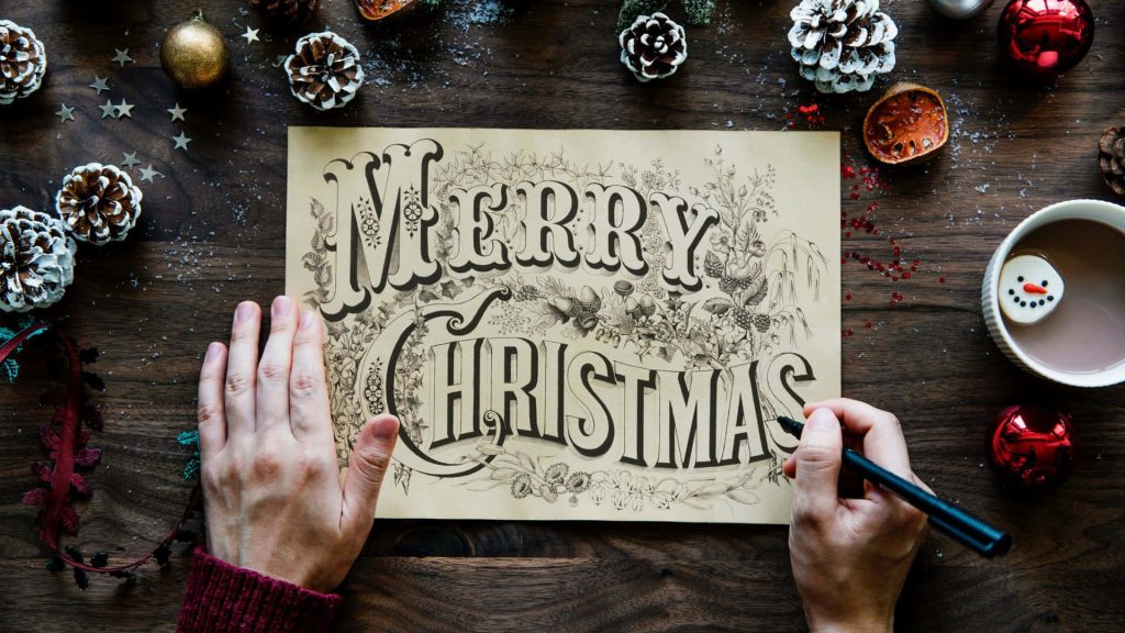 Cozy Christmas overhead shot hand lettering Merry Christmas on wood with pinecones ornaments cocoa Wallpaper