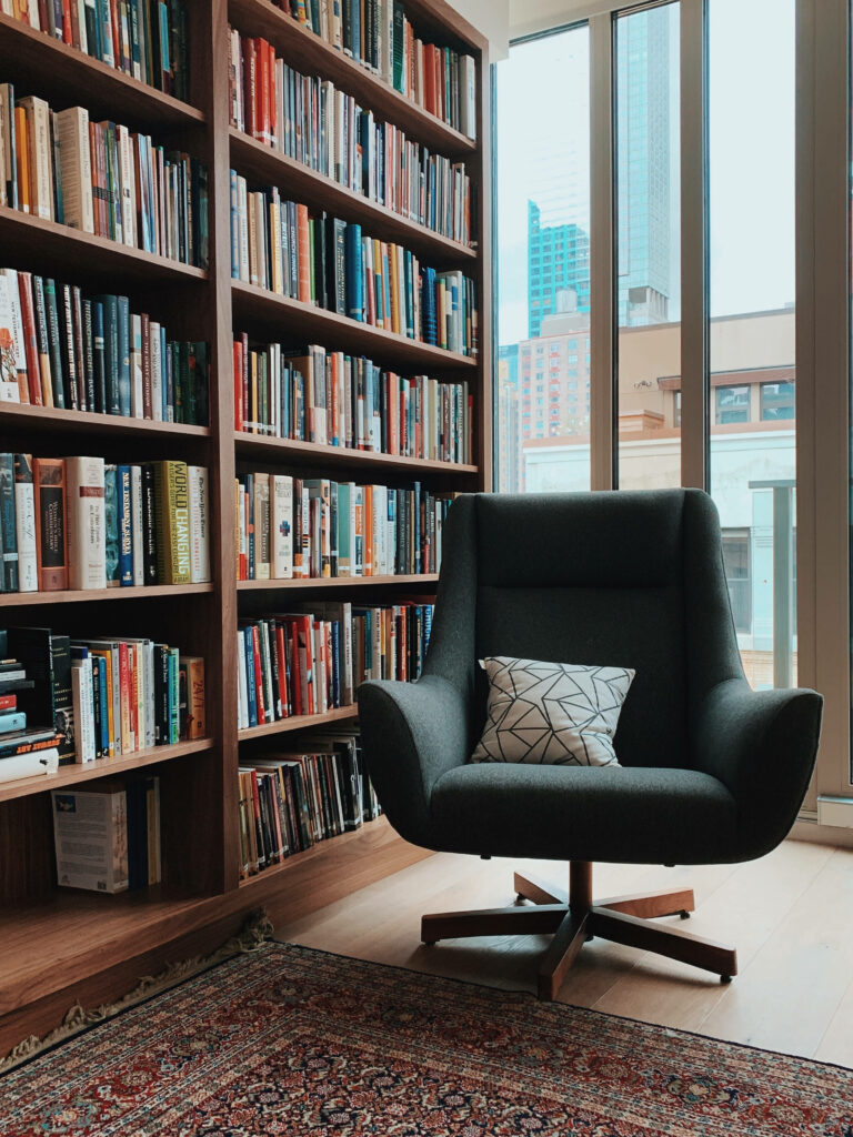 Modern library corner with cozy armchair geometric cushion floor-to-ceiling bookshelves city view Wallpaper