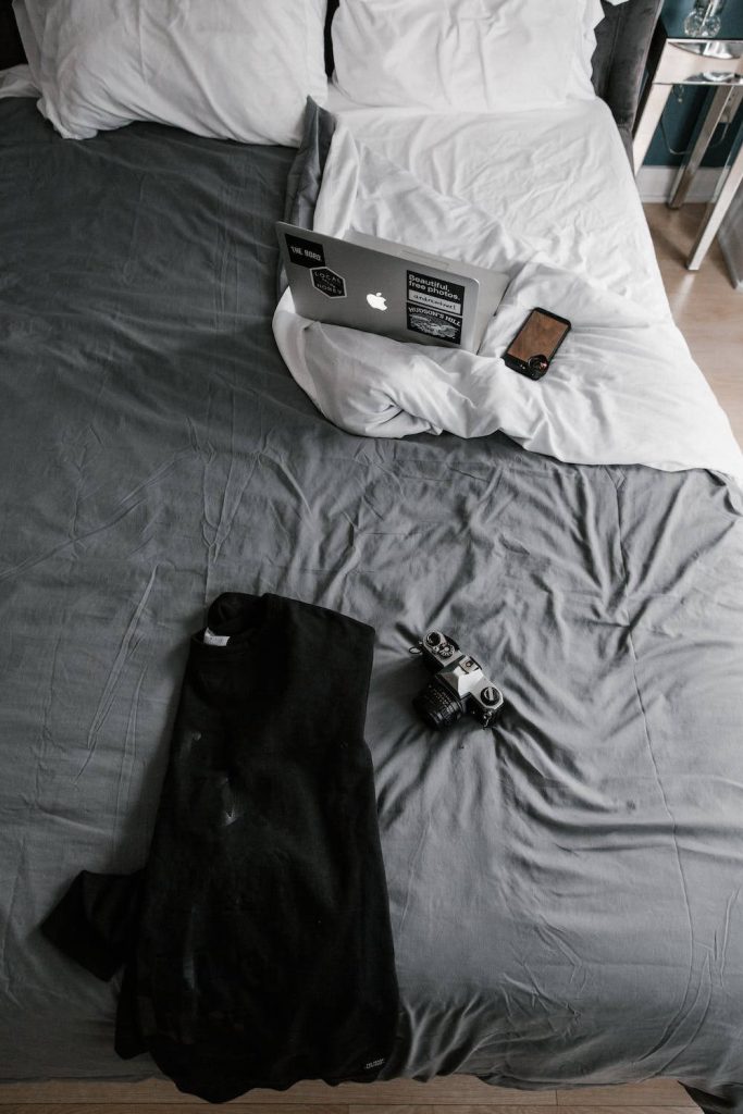 Cozy monochrome flat lay of MacBook vintage camera and phone on gray bed workspace wallpaper