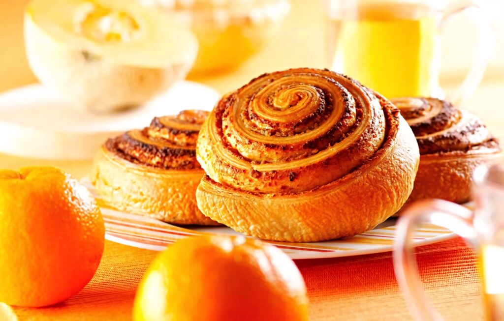 Fresh cinnamon rolls on striped plate with oranges bright cozy breakfast table setting Wallpaper