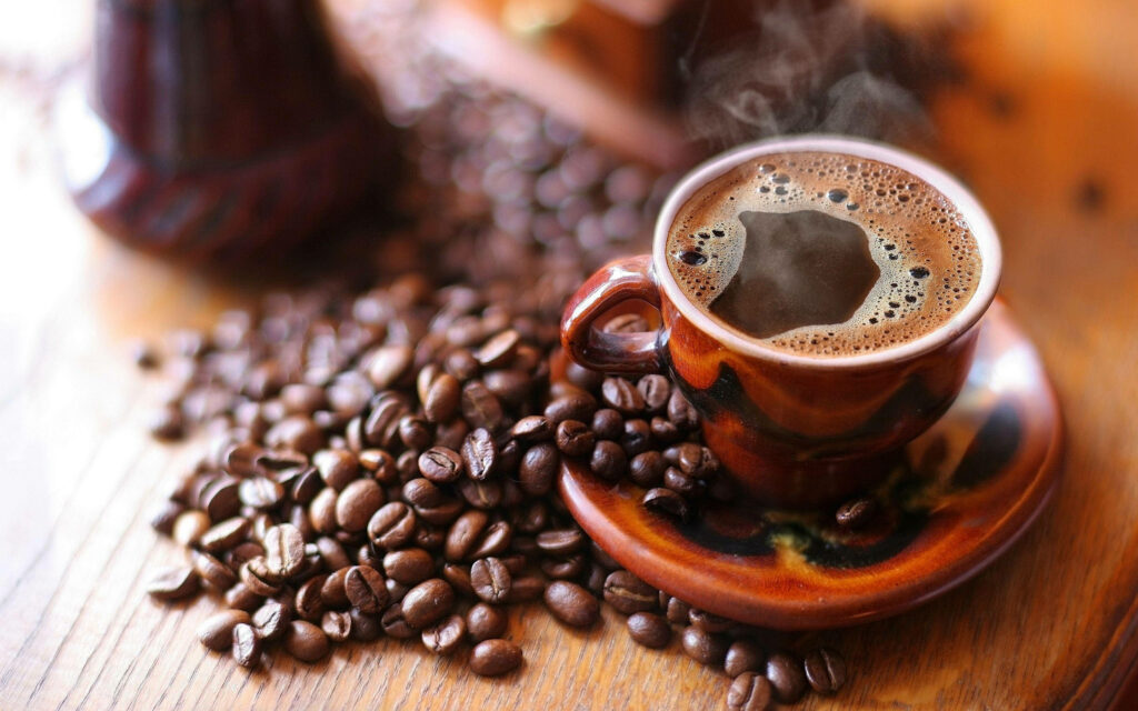 Steaming coffee cup on rustic wooden table with coffee beans cozy warm morning atmosphere wallpaper