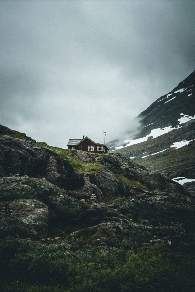 Cozy mountain house on rugged rocks surrounded by mist and snow in serene natural landscape Wallpaper