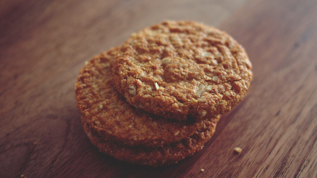 Close-up of three golden oatmeal cookies stacked on rustic wood highlighting crisp texture Wallpaper