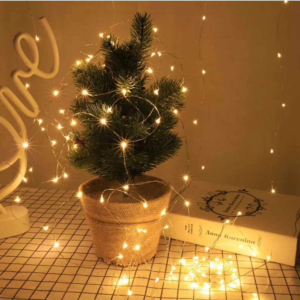 Cozy small potted pine tree wrapped in warm fairy lights on checkered table near book wallpaper