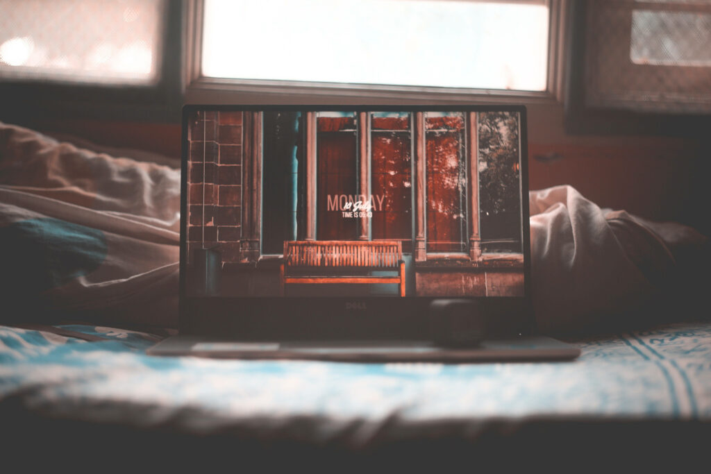 Cozy Vibes: An Indie Aesthetic Laptop Wallpaper featuring an Open Laptop on a Bed with a Charming Wooden Bench Background