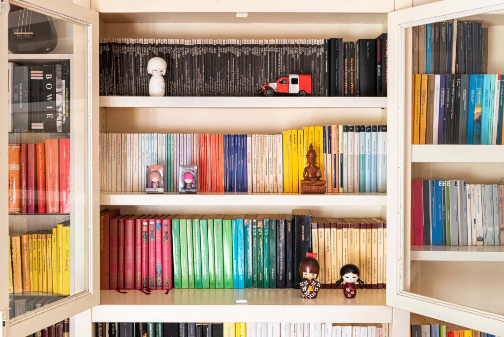 Bright organized bookshelf Zoom background with color books Kokeshi dolls Buddha statue truck Wallpaper