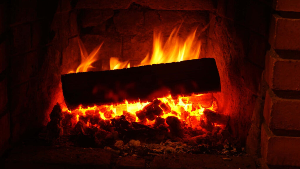 Crackling log fire burning in rustic brick fireplace warm cozy glowing wallpaper background