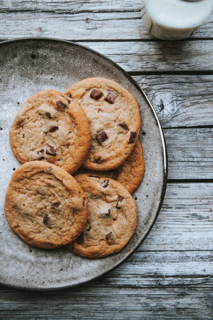 Rustic wallpaper of chocolate chip cookies on ceramic plate with weathered wooden table background